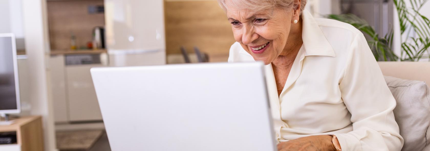 Elderly lady working with laptop. Portrait of beautiful older woman working laptop computer indoors. Senior woman using laptop at home, laughing