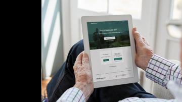 Elderly man holding electronic tablet viewing "Find a Medicare Plan"