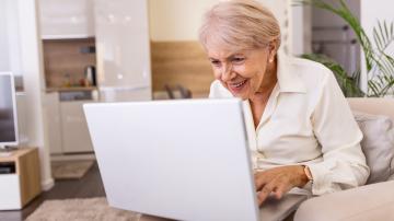 Elderly lady working with laptop. Portrait of beautiful older woman working laptop computer indoors. Senior woman using laptop at home, laughing