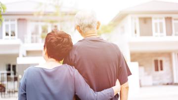 Happy senior couple from behind looking at front of house and car. Warm tone with sunlight