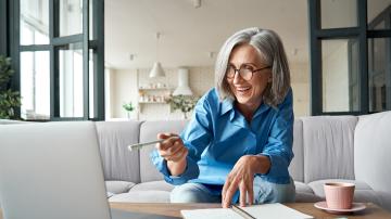 Happy mature older woman video calling on laptop working from home