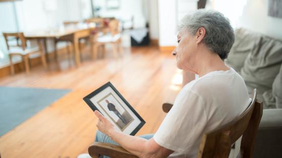 Sad Elderly Woman Sitting on a Chair while Looking at a Picture Frame