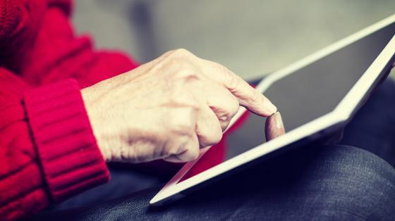 An elderly woman browsing the internet with a tablet in a living room and sitting in a sofa. Image has a vintage effect.