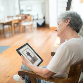 Sad Elderly Woman Sitting on a Chair while Looking at a Picture Frame