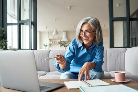 Happy mature older woman video calling on laptop working from home